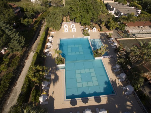 Piscina a forma di L circondata da ombrelloni e piante.