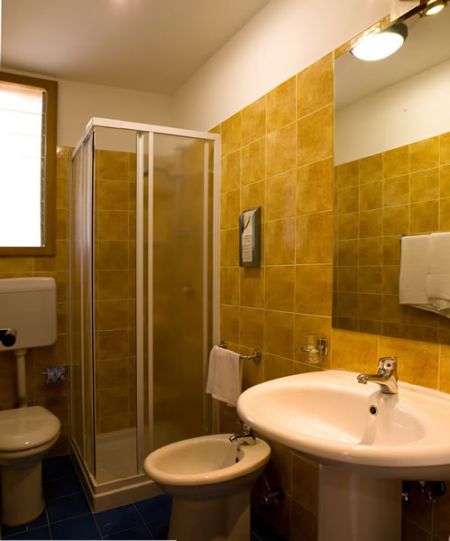 Bagno con piastrelle gialle, box doccia, lavabo e bidet.