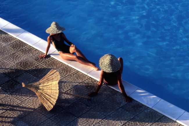 Due persone con cappelli di paglia siedono vicino a una piscina.