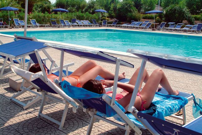 Due persone sdraiate su lettini vicino a una piscina.