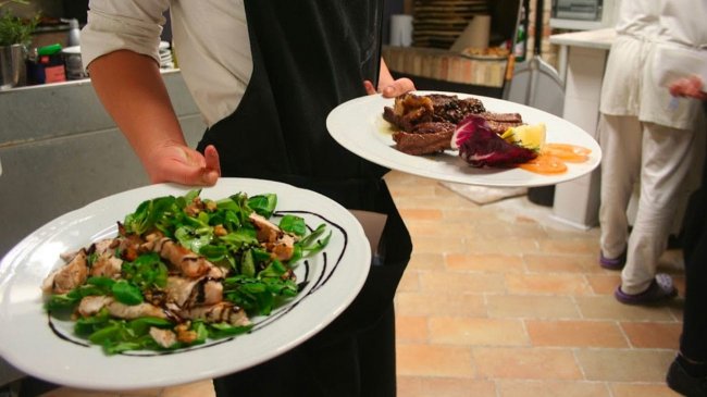 Cameriere serve piatti di carne e insalata.