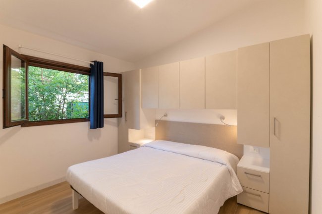 Camera con letto matrimoniale, mobili chiari e finestra aperta su giardino.