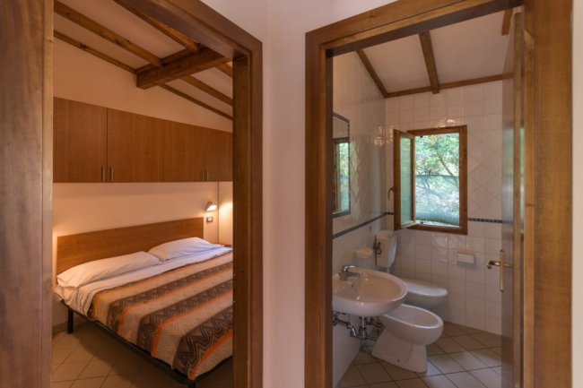 Vista su camera da letto e bagno, entrambi con finestra aperta e finiture in legno.