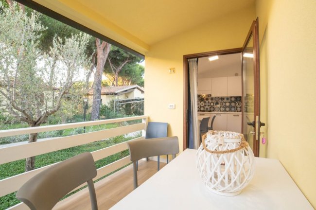 Balcone con tavolo bianco e vista su alberi, accesso a cucina.