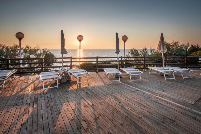 Terrazza in legno con lettini e ombrelloni, vista mare al tramonto.