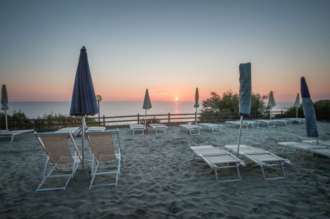 Spiaggia con lettini e ombrelloni chiusi, il mare al tramonto.