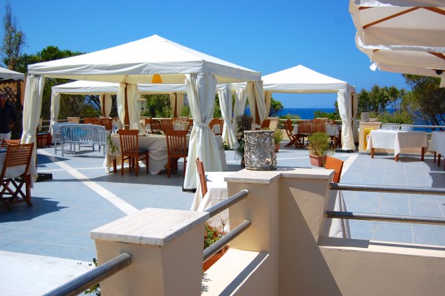 Tavoli e sedie sotto gazebo bianchi su una terrazza vista mare, con cielo blu.