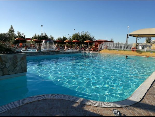 Piscina all'aperto con acqua azzurra, ombrelloni e sdraio.