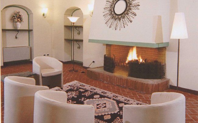 Un salotto con camino acceso, sedie bianche e tappeto decorato.