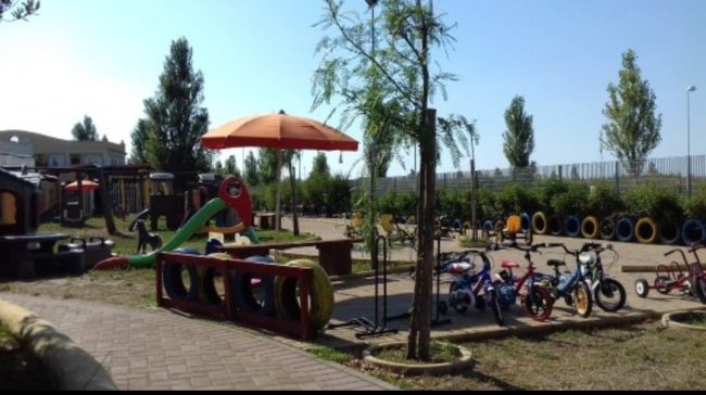 Un parco giochi con biciclette, scivolo e ombrellone arancione.