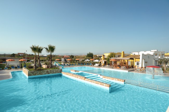 Piscina con palme e strutture residenziali sullo sfondo.