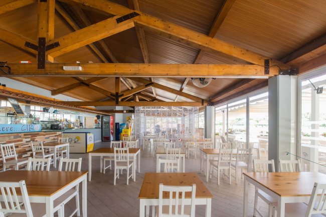 Un ristorante con tavoli e sedie bianche sotto un soffitto di legno.