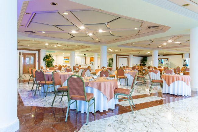 Sala da pranzo con tavoli apparecchiati e sedie attorno.