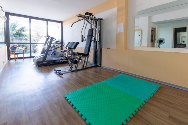 Palestra con attrezzi, tapis roulant e tappetino verde.