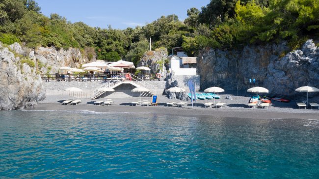 Spiaggia rocciosa con ombrelloni e sedie.