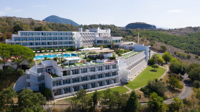 Resort bianco con piscine, circondato da colline verdi.