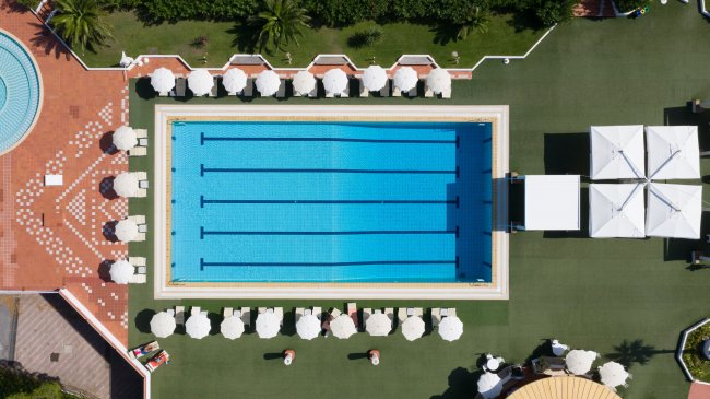 Vista dall'alto di una piscina rettangolare circondata da ombrelloni bianchi.