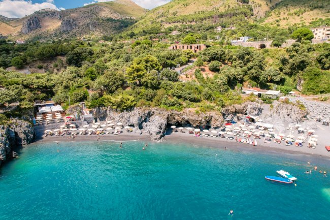 Spiaggia vista dall'alto con mare e ombrelloni.