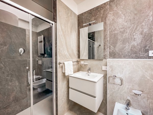 Bagno elegante con doccia in vetro, lavabo moderno e rivestimenti in pietra.