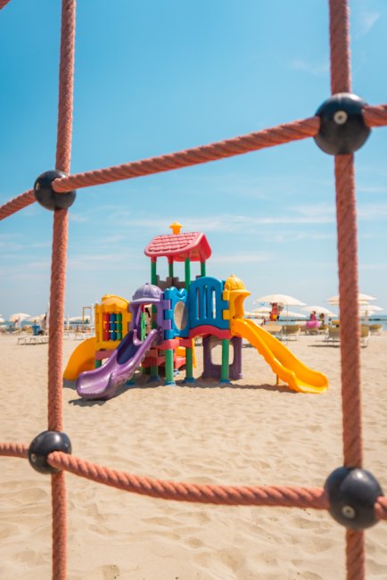 Un colorato parco giochi sulla sabbia, visto attraverso una rete di corda.