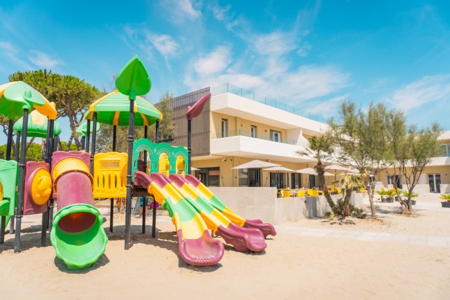 Area giochi colorata in spiaggia davanti a un edificio moderno, cielo sereno.
