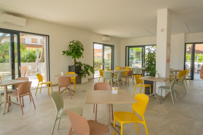 Sala interna con tavoli e sedie colorate, piante decorative.