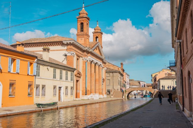Edifici storici e canale con ponte e cielo parzialmente nuvoloso.