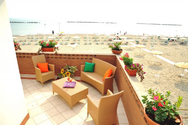Terrazza con arredi e fiori affacciata su una spiaggia con ombrelloni.