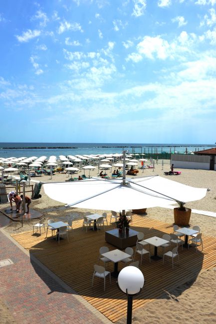 Area all'aperto con tavoli e ombrelloni su una spiaggia soleggiata.
