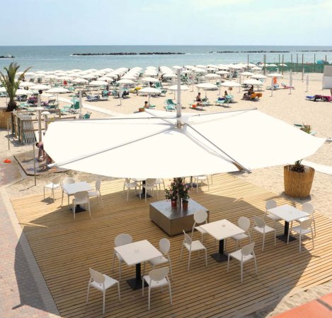 Area con tavoli e sedie sotto un grande ombrellone bianco sulla spiaggia.