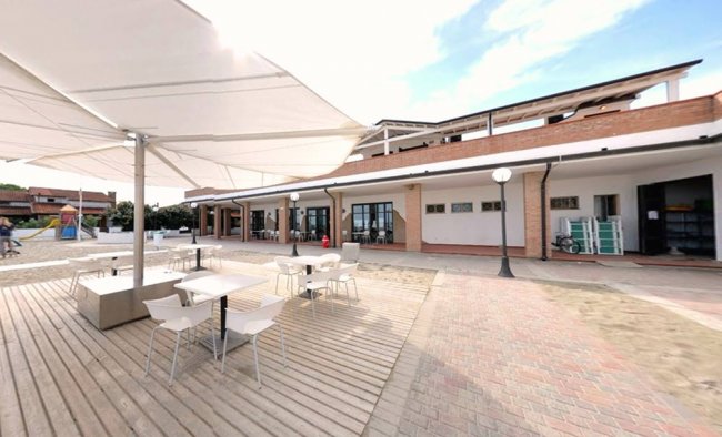 Area esterna con tavoli, sedie e ombrelloni bianchi fuori da un edificio.