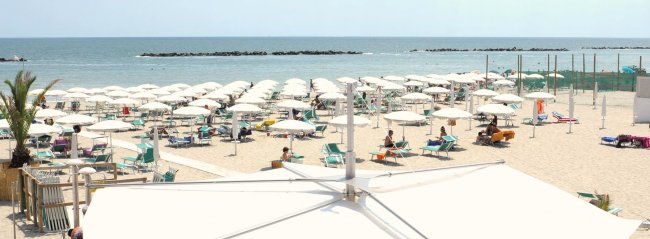 Spiaggia con ombrelloni bianchi e lettini verdi vicino al mare.
