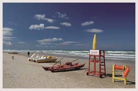 Spiaggia con pedalò, canoa e attrezzature di salvataggio sulla sabbia.