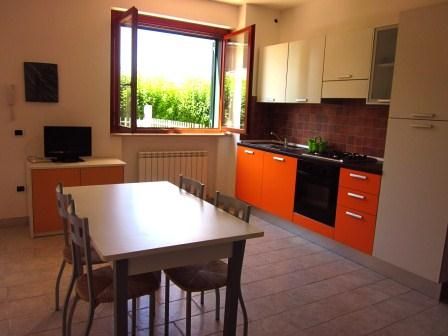 Cucina moderna con mobili arancioni, tavolo, sedie, e finestra aperta.