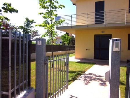 Ingresso di una casa con giardino e una porta. Cancelletto aperto verso un vialetto.