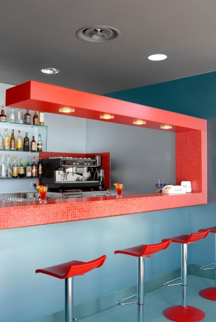 Interno di un bar moderno con bancone rosso, sgabelli e una macchina da caffè.