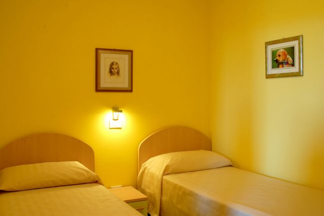 Due letti singoli in una stanza gialla con quadri alle pareti.