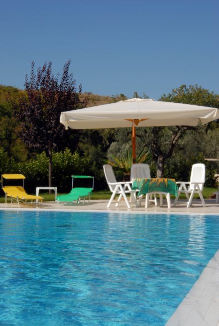 Piscina luminosa con lettini colorati e ombrellone bianco, immersa nel verde.