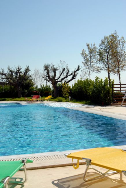 Piscina con sedie a sdraio colorate e alberi sullo sfondo.