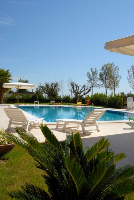 Piscina all'aperto con lettini bianchi, ombrelloni e vegetazione intorno.