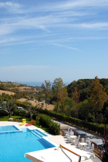 Piscina con vista su colline verdi e mare in lontananza.