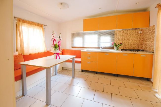 Cucina luminosa con mobili arancioni, tavolo bianco e sedute. Fiori sul tavolo.