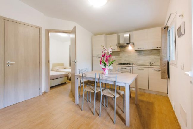 Cucina moderna con tavolo in legno e sedie. Porta aperta su una camera da letto.