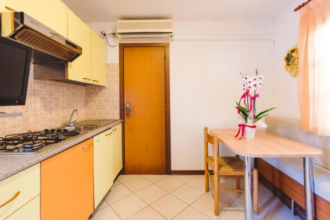 Cucina con mobili gialli e arancioni, tavolo in legno con fiori e porta di legno.