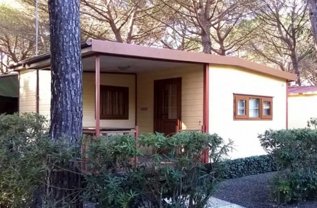 Una casetta di legno in un'area boschiva con ampio portico e finestre.