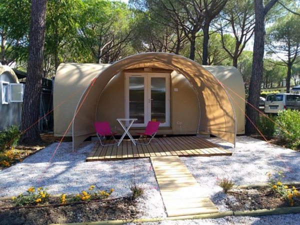 Tenda moderna con terrazza in legno e sedie davanti, circondata da alberi.