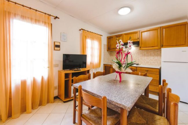 Cucina accogliente con tavolo in pietra, TV e mobili in legno chiaro.