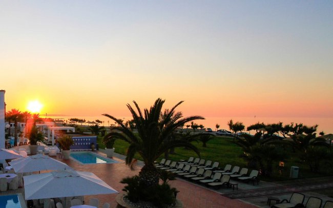 Tramonto su un resort con piscina, palme e sedie a sdraio.