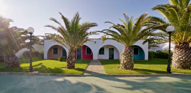 Edificio bianco con porte colorate e palme davanti.