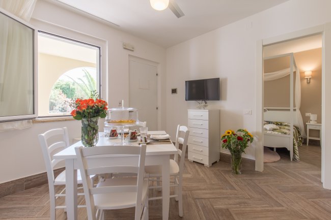 Sala da pranzo luminosa con tavolo bianco e TV a parete.